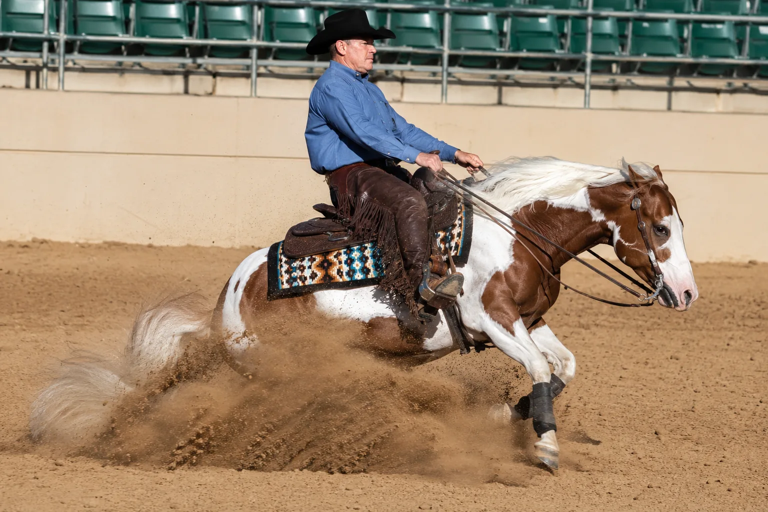 American Paint Horse in full action during a reining slide stop, kicking up dust in an arena, with a Western rider.